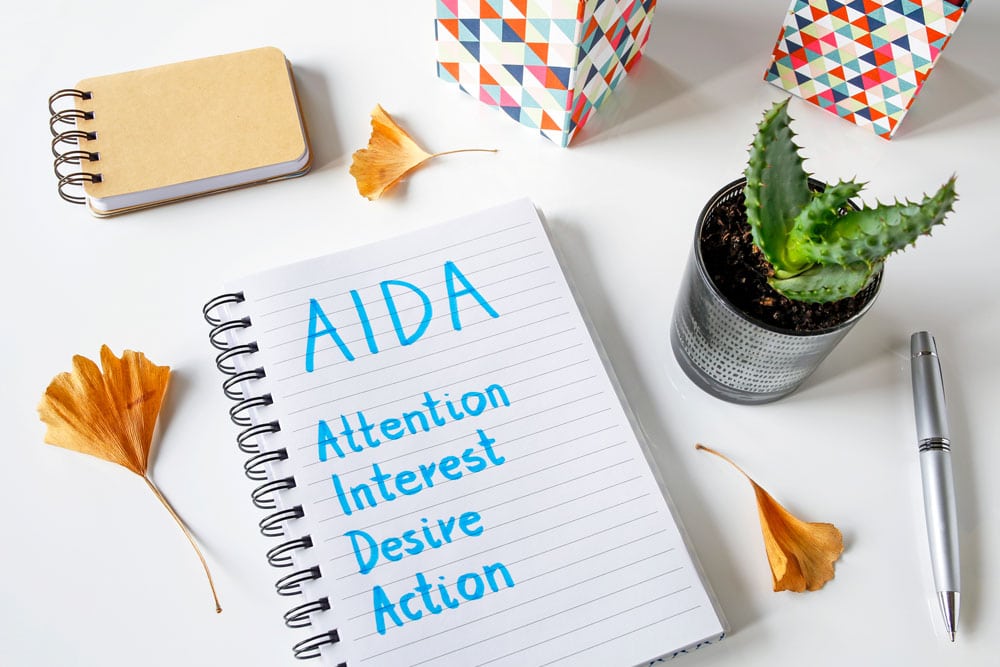 Conversion Funnel Marketing: 7 Steps To Success 2 Notebook reads AIDA - Attention, Interest, Desire, Action for Sales Funnel marketing