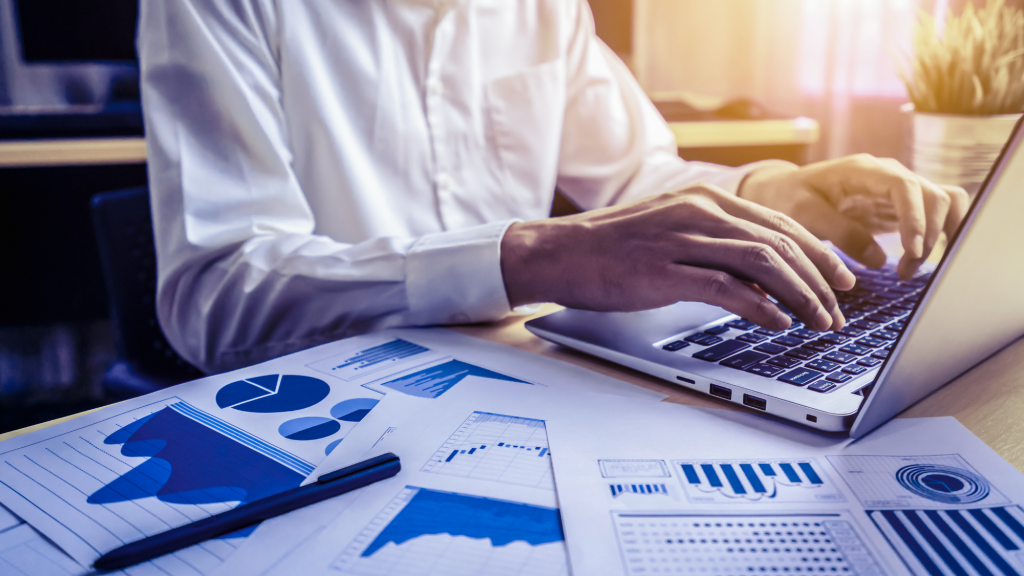 A man typing on a laptop while viewing graphs, brainstorming advertising ideas.