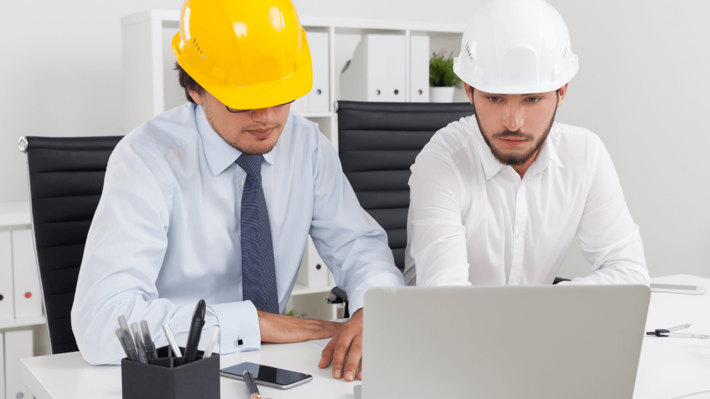 Two construction workers discussing marketing ideas while examining a laptop.