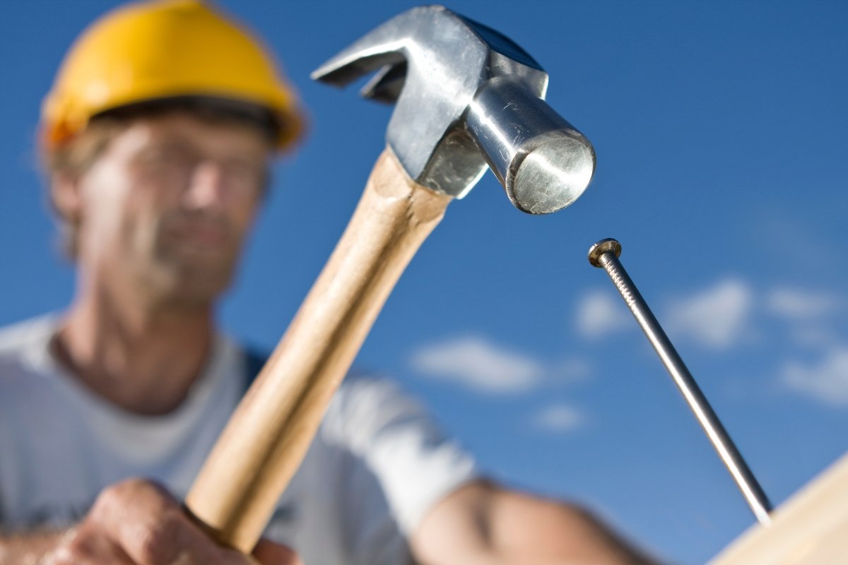 A construction worker with a hammer on top of wood demonstrates local roofing company expertise.