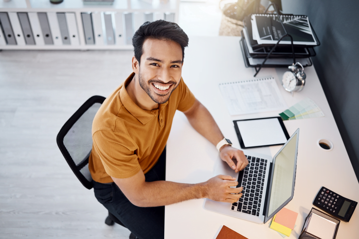 A smiling man sitting at a desk with a laptop, comparing Wix vs WordPress for SEO.