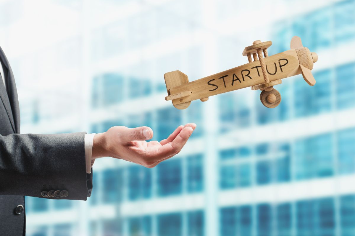 A businessman's hand holding a wooden airplane with the word startup on it, representing innovative marketing strategies for startups.