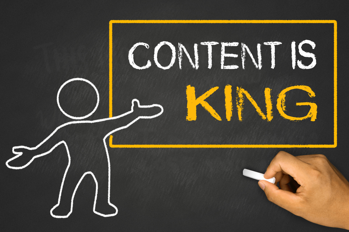 A person writing the word "content is king" on a chalkboard, emphasizing its significance for small businesses.