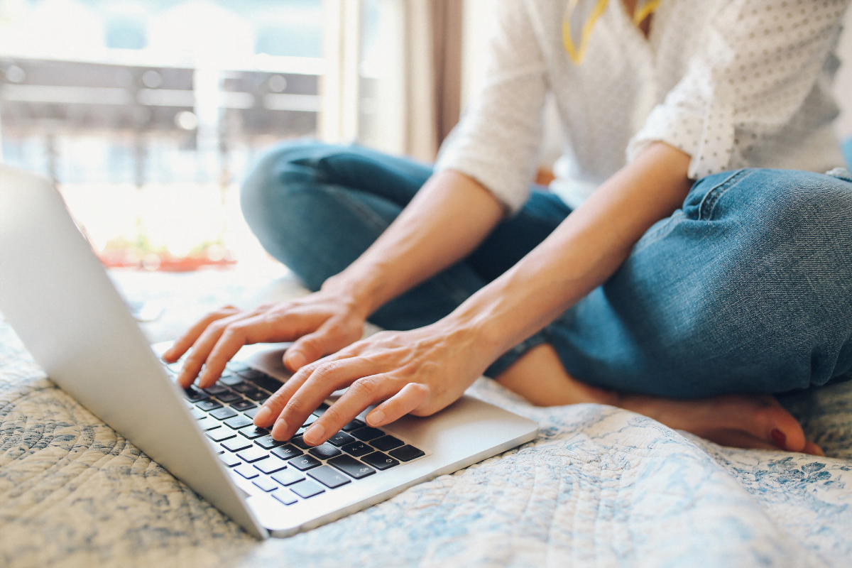 A woman typing on a laptop on a bed, crafting persuasive copy that converts.