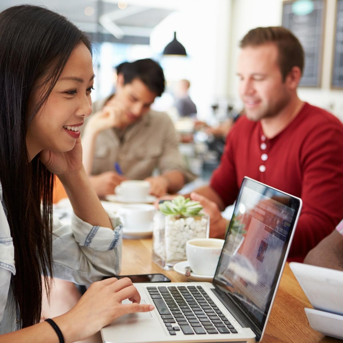 A customer avatar participating in a meeting with colleagues at a table, each using laptops.