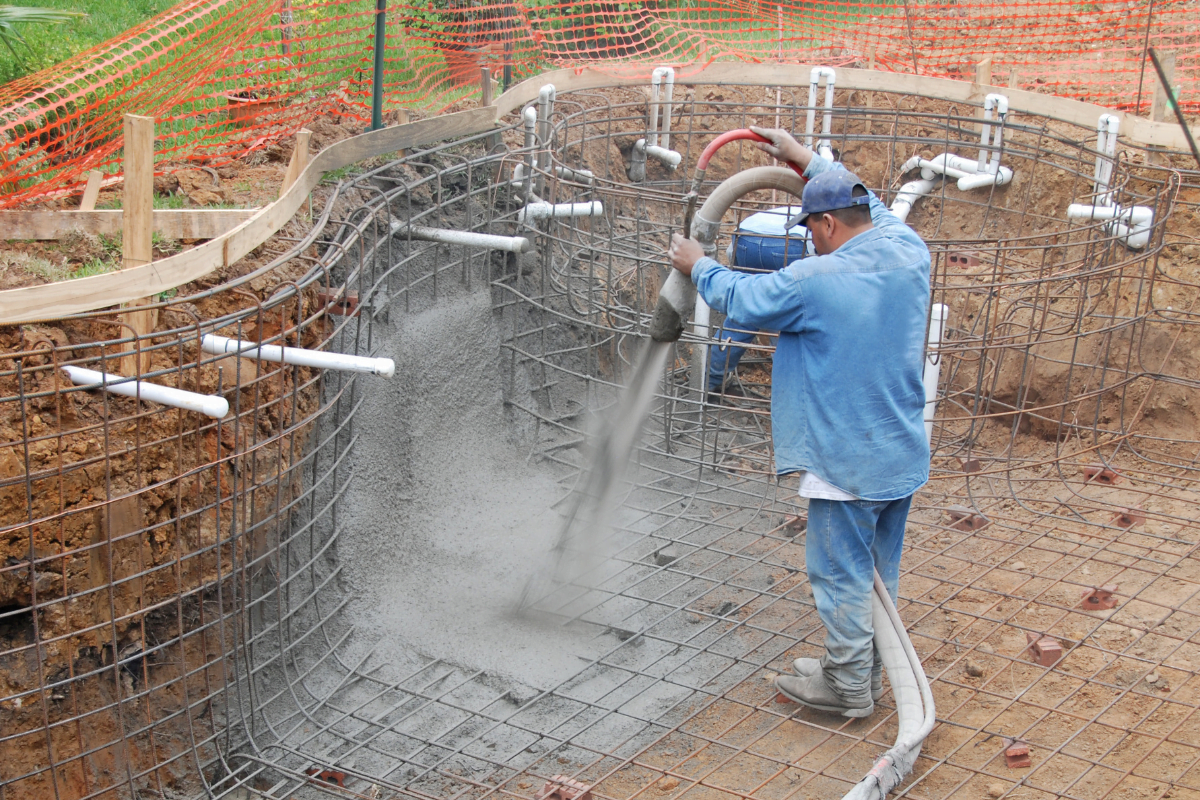 A pool builder pouring concrete into a pool.
