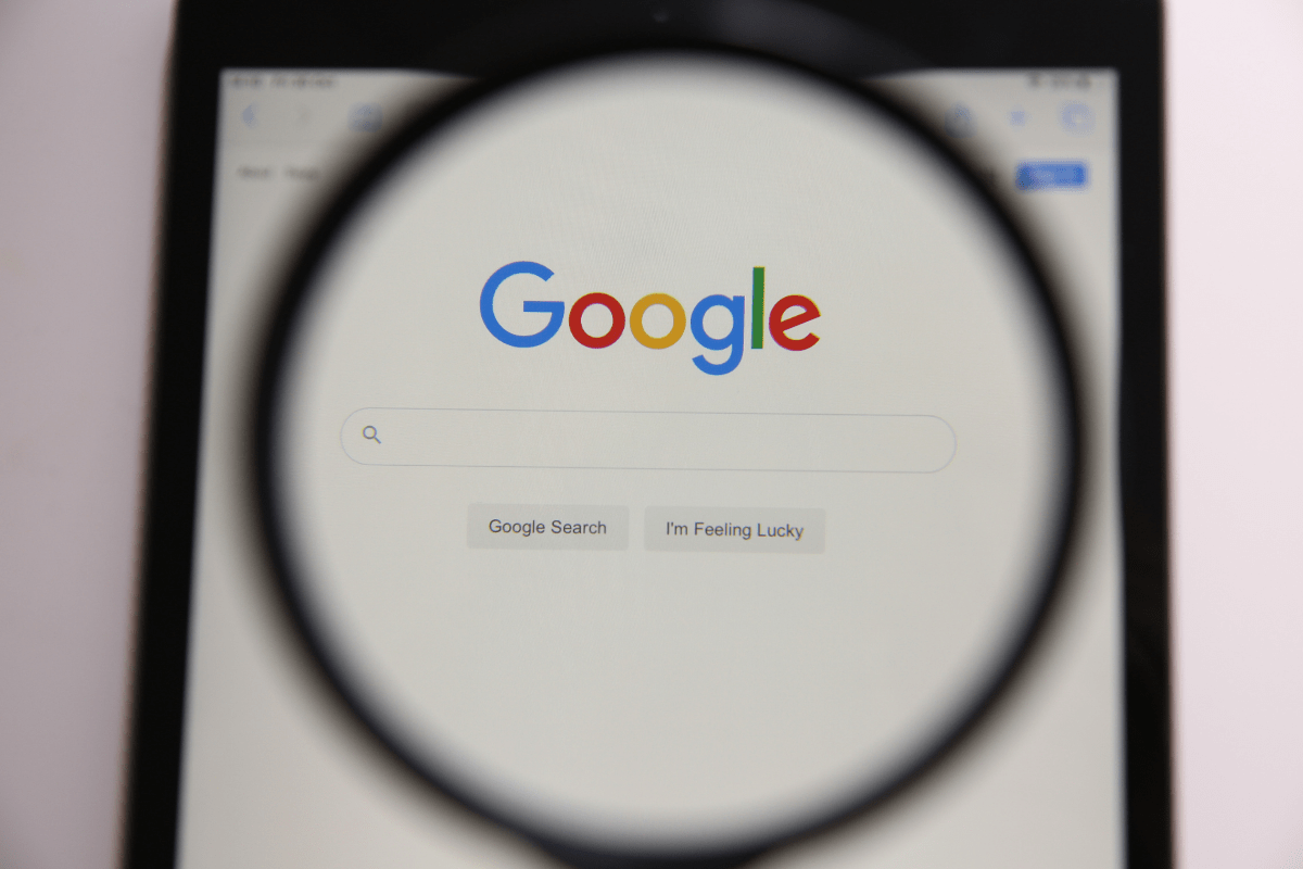A magnifying glass on top of a tablet computer with Google on the screen.