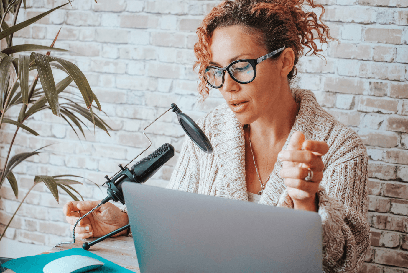 A digital creator sits at a desk with a laptop and microphone.