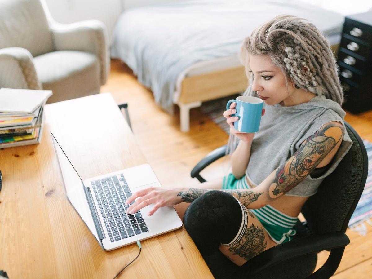 A tattooed woman at a desk with a laptop and a cup of coffee, creating a content outline.