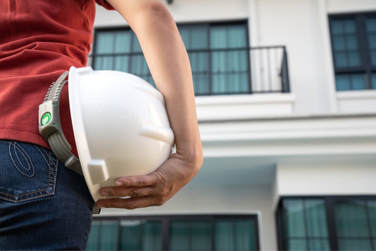 A woman holding a hard hat in front of a house for a home builder.