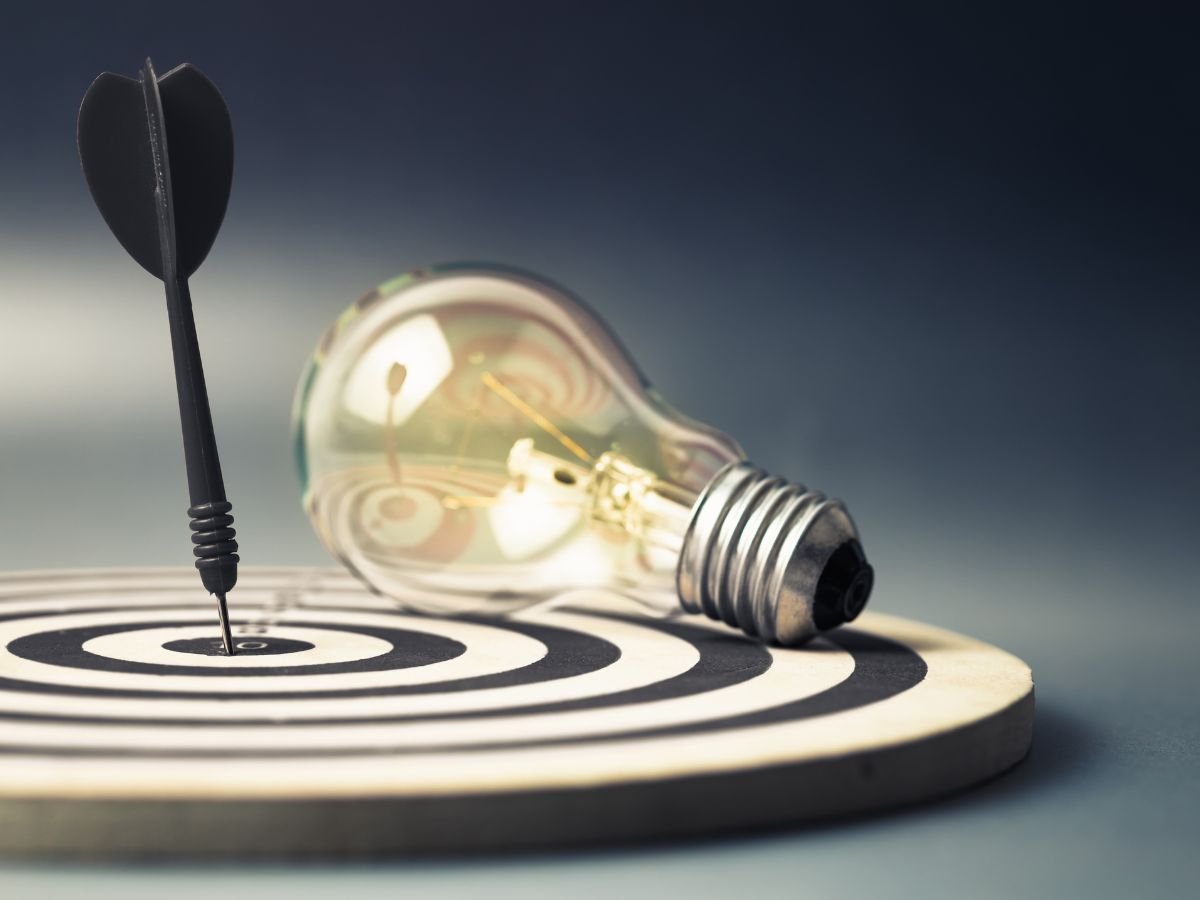 A target centered with a light bulb and a dart exemplifying the concept of smart goals.