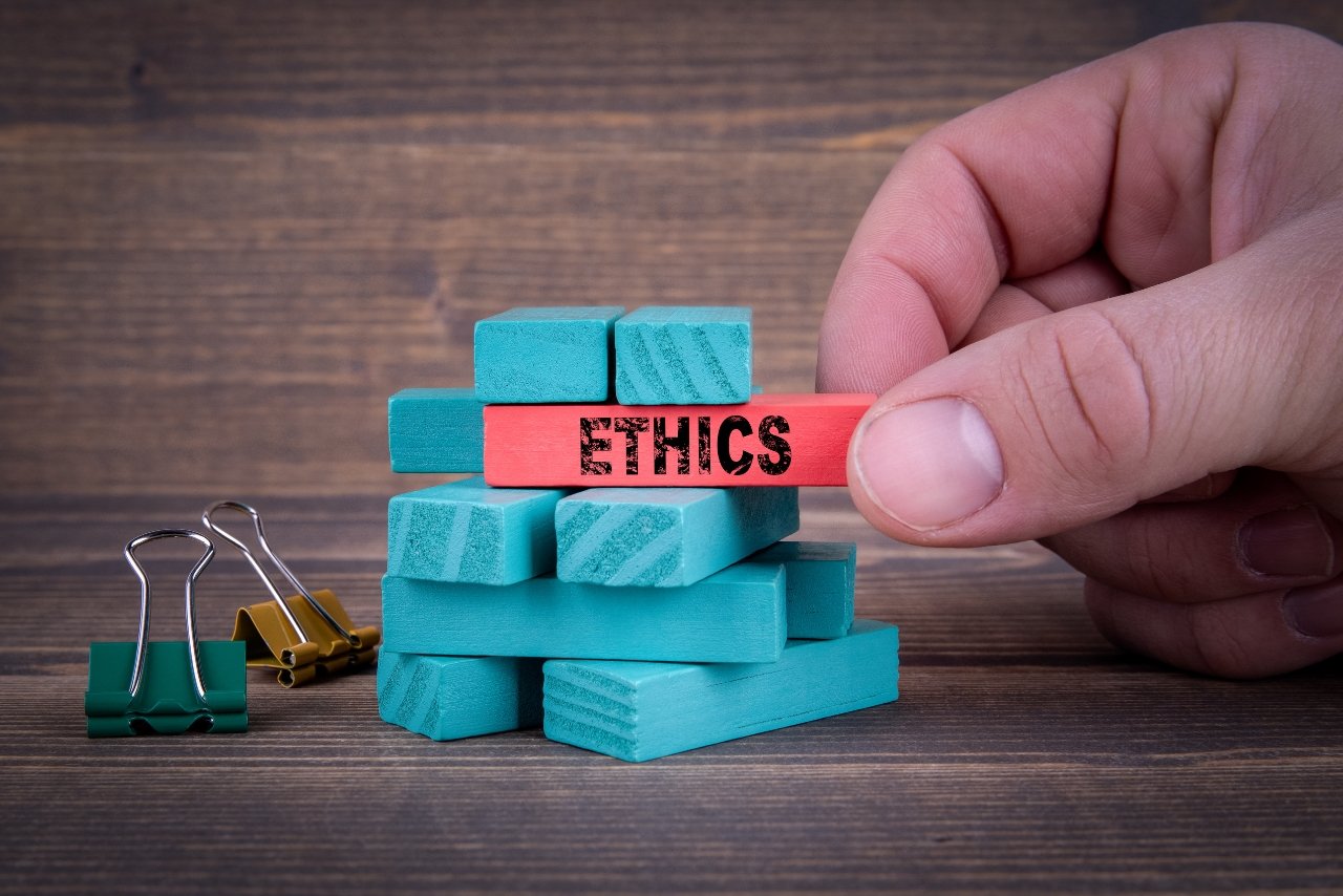 A hand holding a wooden block with the word ethics on it, addressing ethical marketing issues.