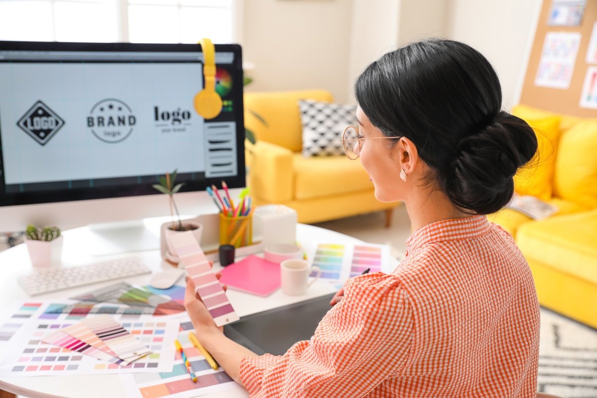 A woman is using a computer in her home office to create a logo.