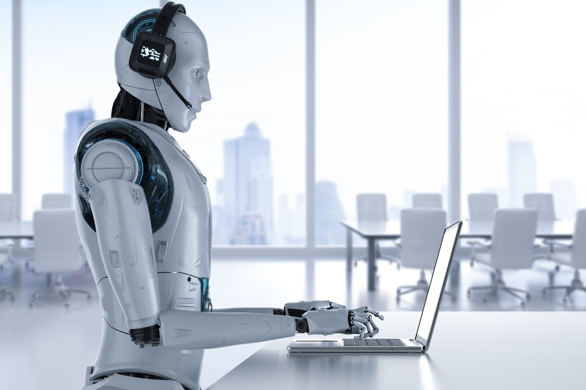 A chatbot robot sitting at a desk using a laptop.