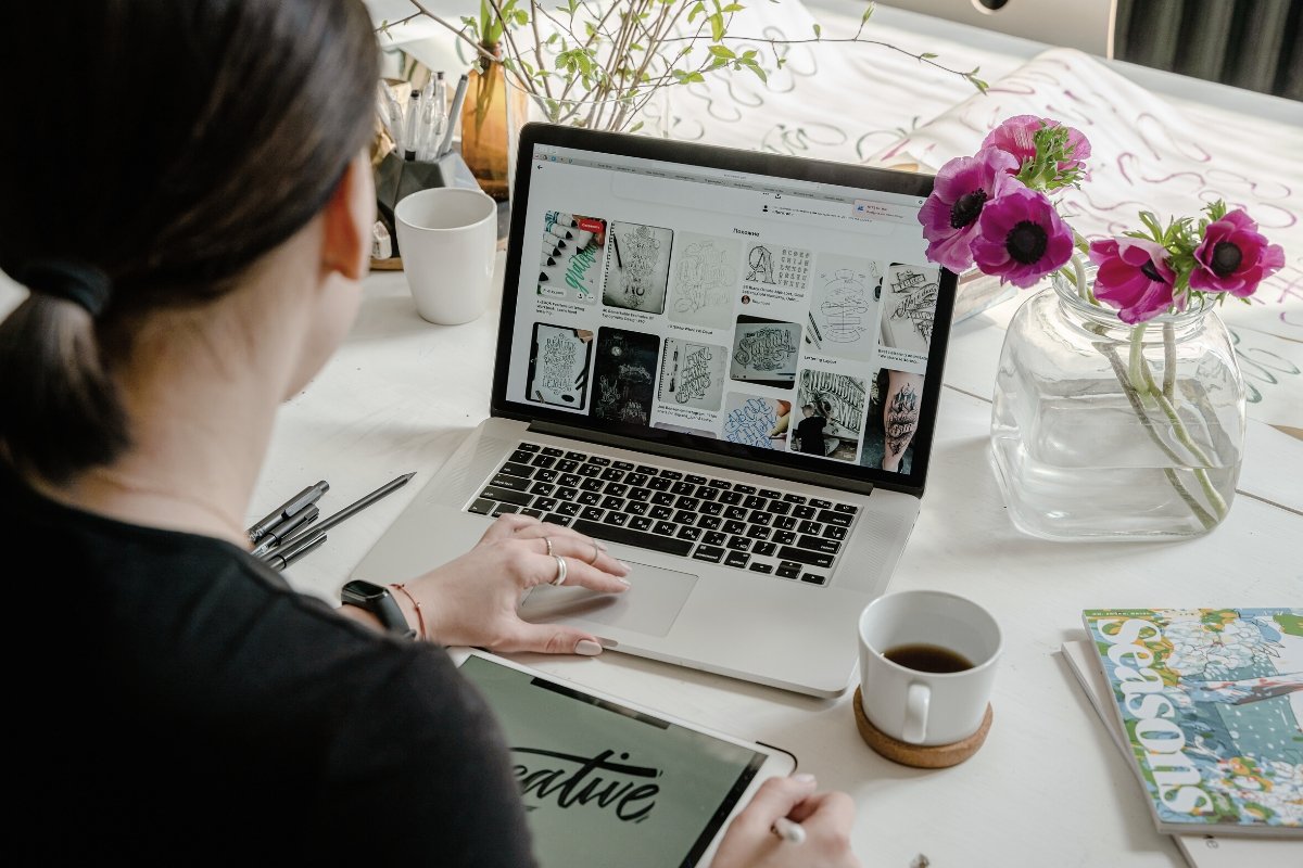 A woman overseeing a website revamp while seated at a desk with a laptop and flowers.