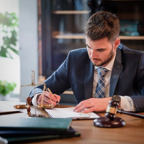 An attorney sitting at a desk, wearing a suit and holding a gavel.