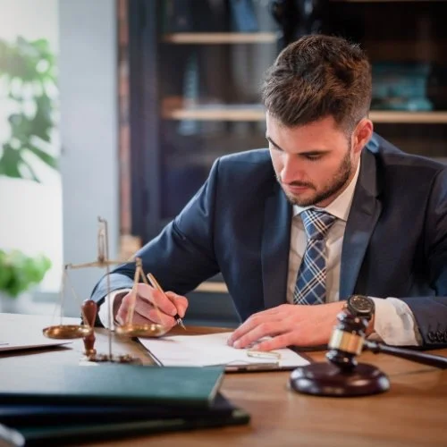 An attorney sitting at a desk, wearing a suit and holding a gavel.