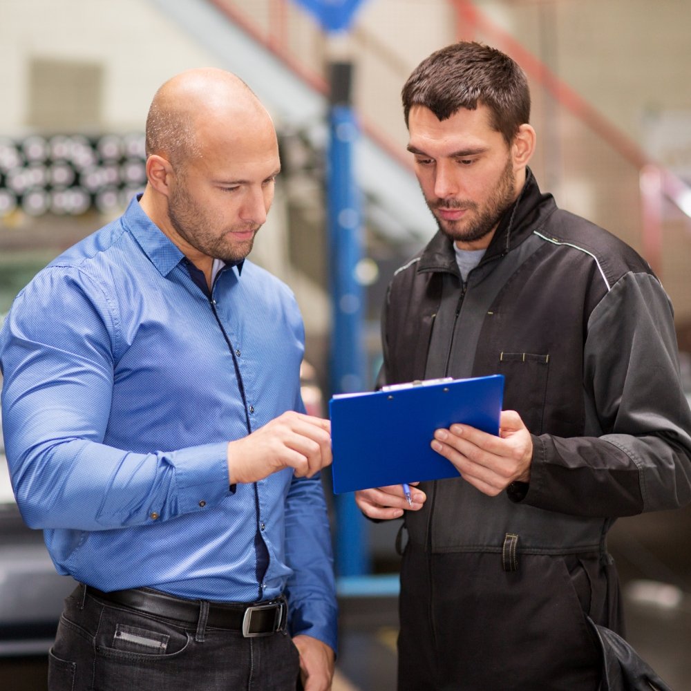 Two mechanics in a garage consulting an automotive marketing agency on a tablet.