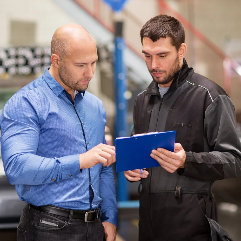 Two mechanics in a garage consulting an automotive marketing agency on a tablet instead of an automotive crm software platform.