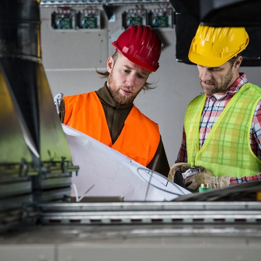 Two construction workers analyzing HVAC blueprints in a factory.