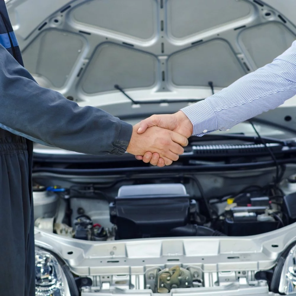 Two mechanics representing an automotive marketing agency sealing a deal in front of a car.