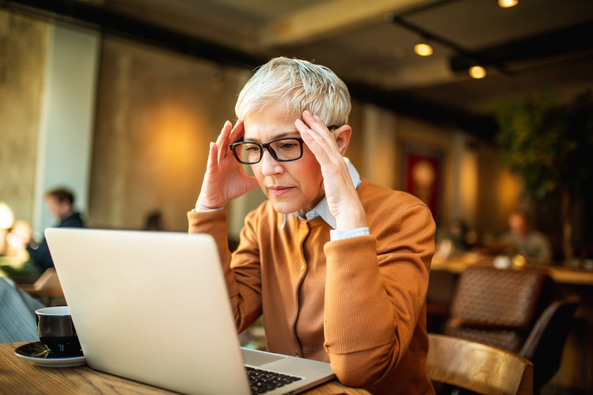 A woman is sitting at a table, visibly distressed and holding her head as she deals with negative comments.