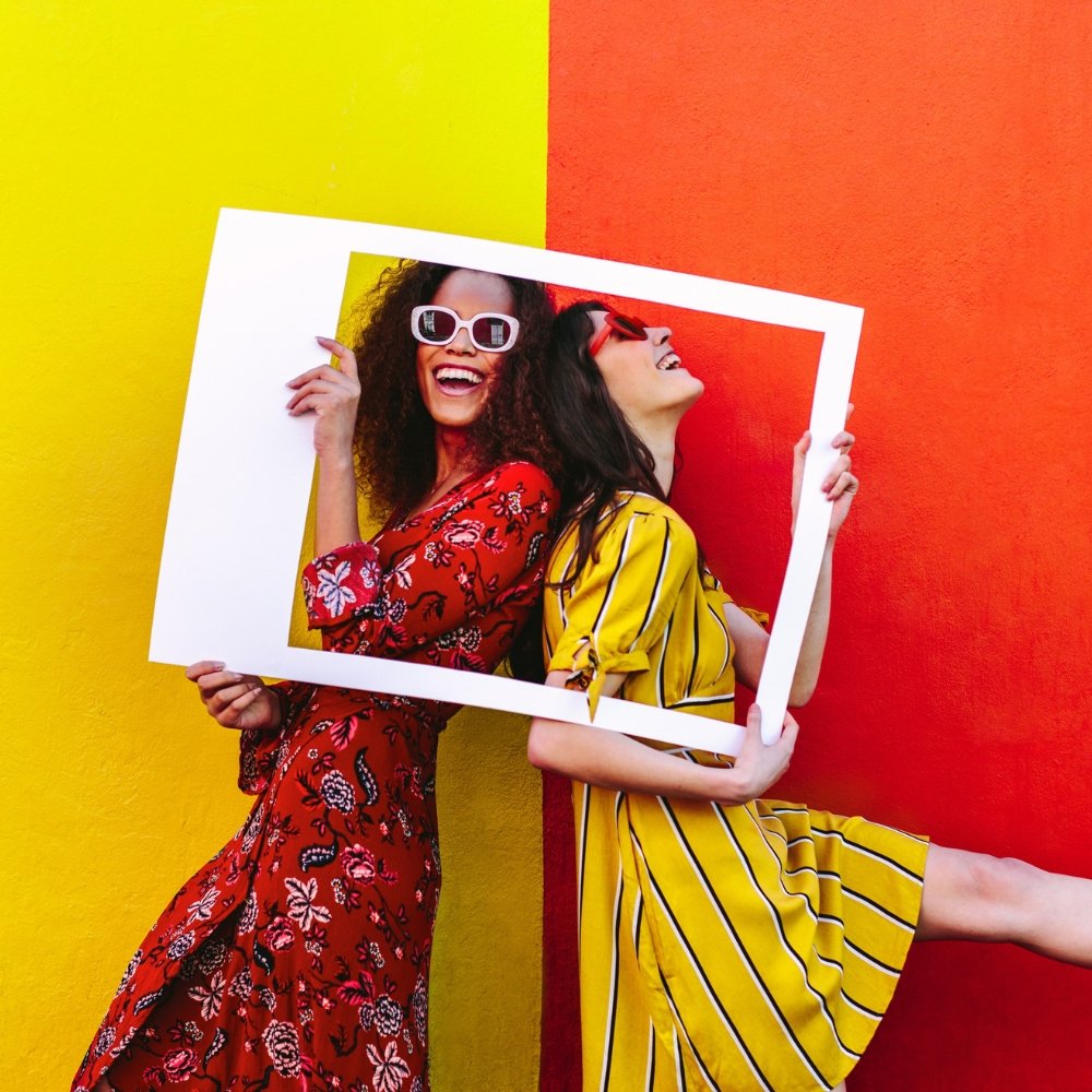 Two women promoting an instagram marketing agency by holding a white frame against a colorful wall.