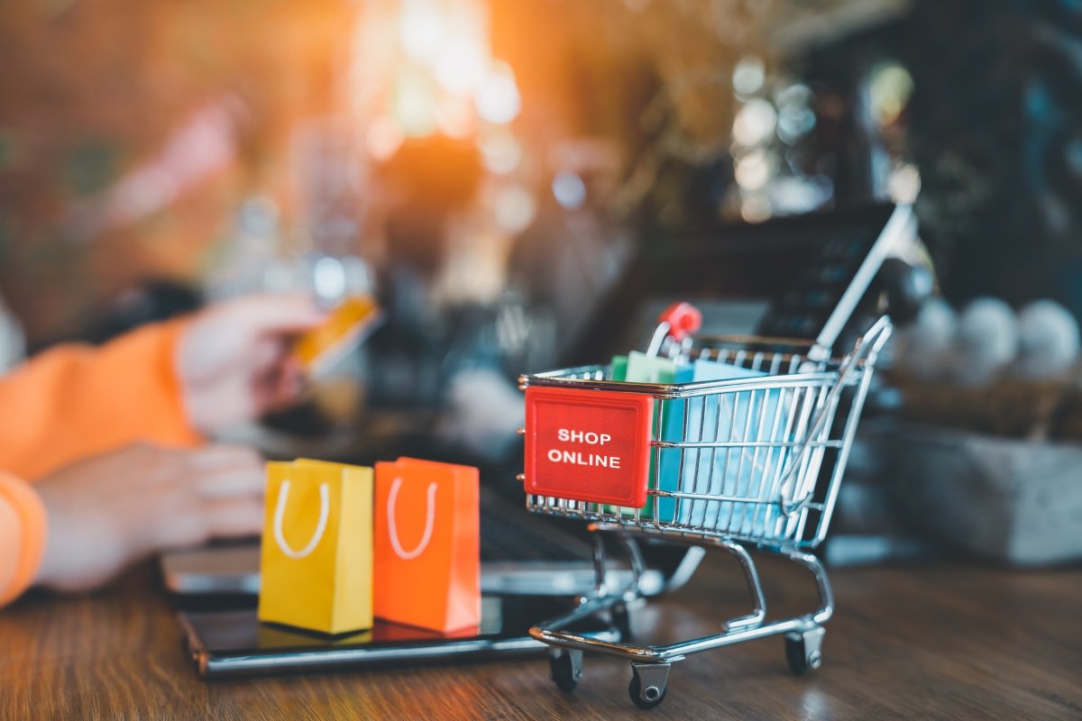 A person comparing Woocommerce and Shopify platforms while holding a shopping cart in front of a laptop.