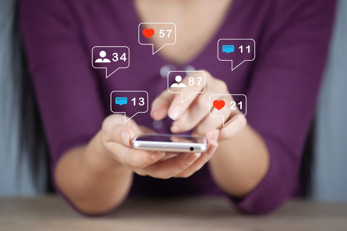 Shadow Banning on Social Media 3 A woman holding a cell phone displaying social icons, unaware of the potential shadow banning.