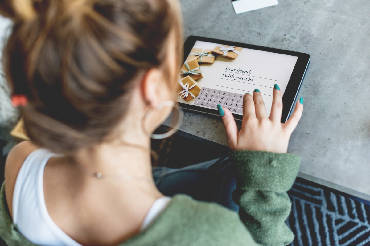 Boost E-Commerce Sales With WooCommerce Gift Cards Plugin 3 A woman is using a tablet adding a message and customizing her WooCommerce gift cards.
