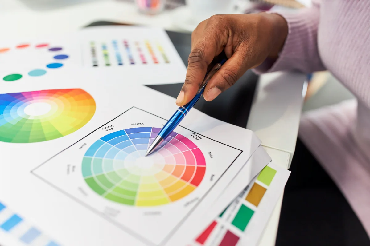 Website Color Schemes That Speak Volumes About Your Brand 3 A woman, seated at a desk, holding a color wheel and examining it alongside a pen in her hand.