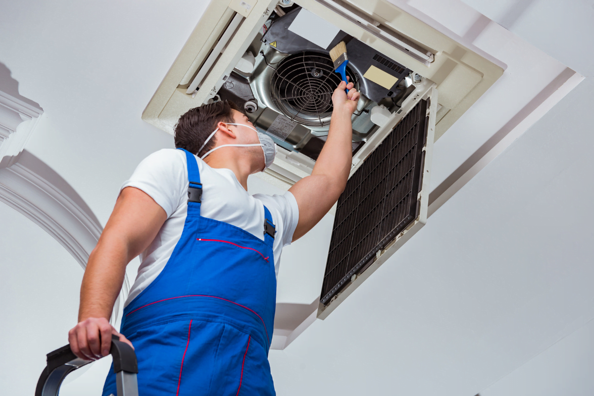 An HVAC technician in overalls is working on an air conditioner.