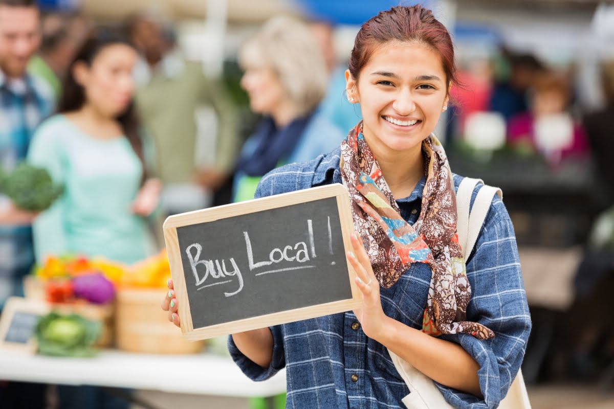 A woman advocating for local businesses by holding up a sign that says "buy local," promoting local store marketing efforts.