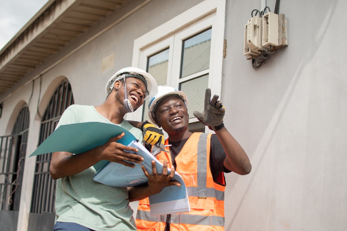 Two construction workers standing in front of a house, showcasing their expertise in electrical installations for SEO.