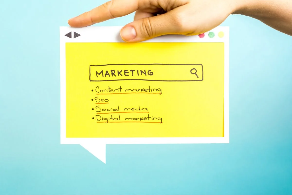 A hand holding a yellow sticky note with the words "SEO" and "marketing" written on it, emphasizing digital marketing strategies.