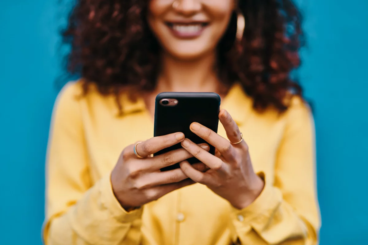 Social Proof Marketing: Boost Your Brand With Trustworthy Validation Techniques 4 A woman with curly hair is happily using a cell phone.