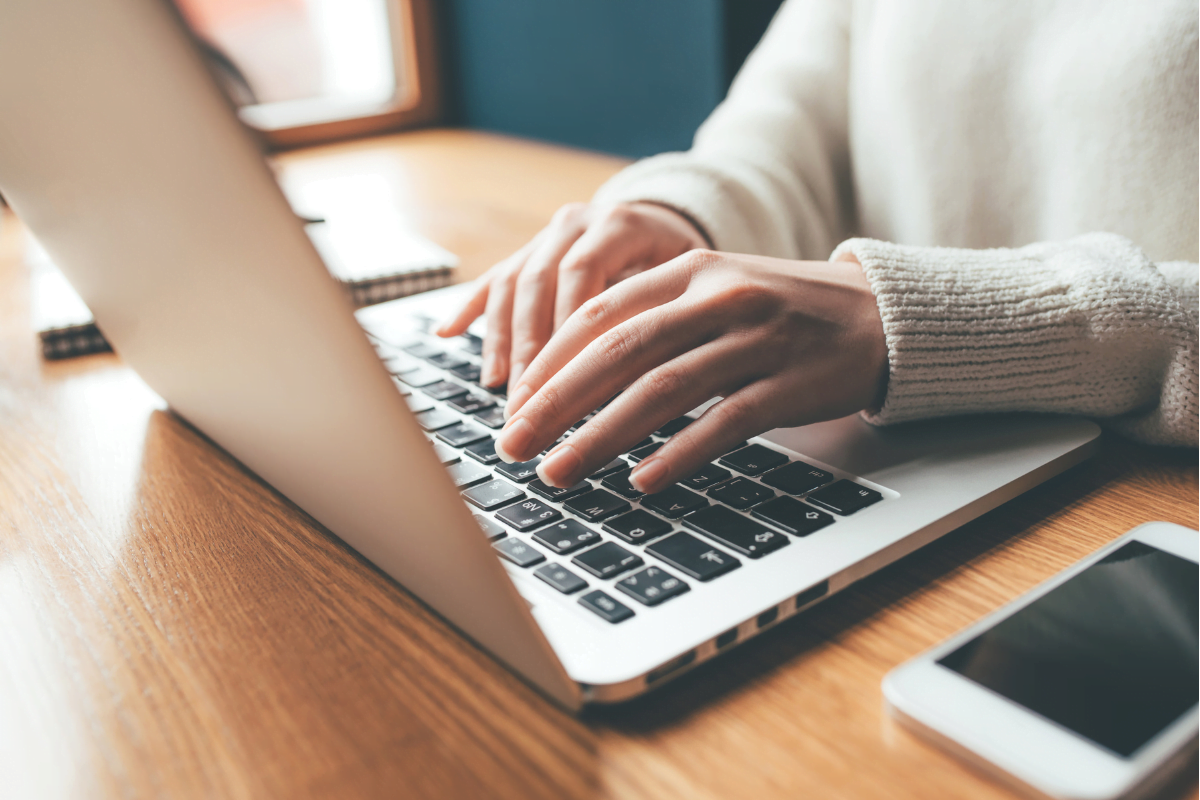 Website Copy 101: Mastering The Art Of Writing Compelling Website Content 1 A woman typing a website copy on a laptop with a cellphone nearby.