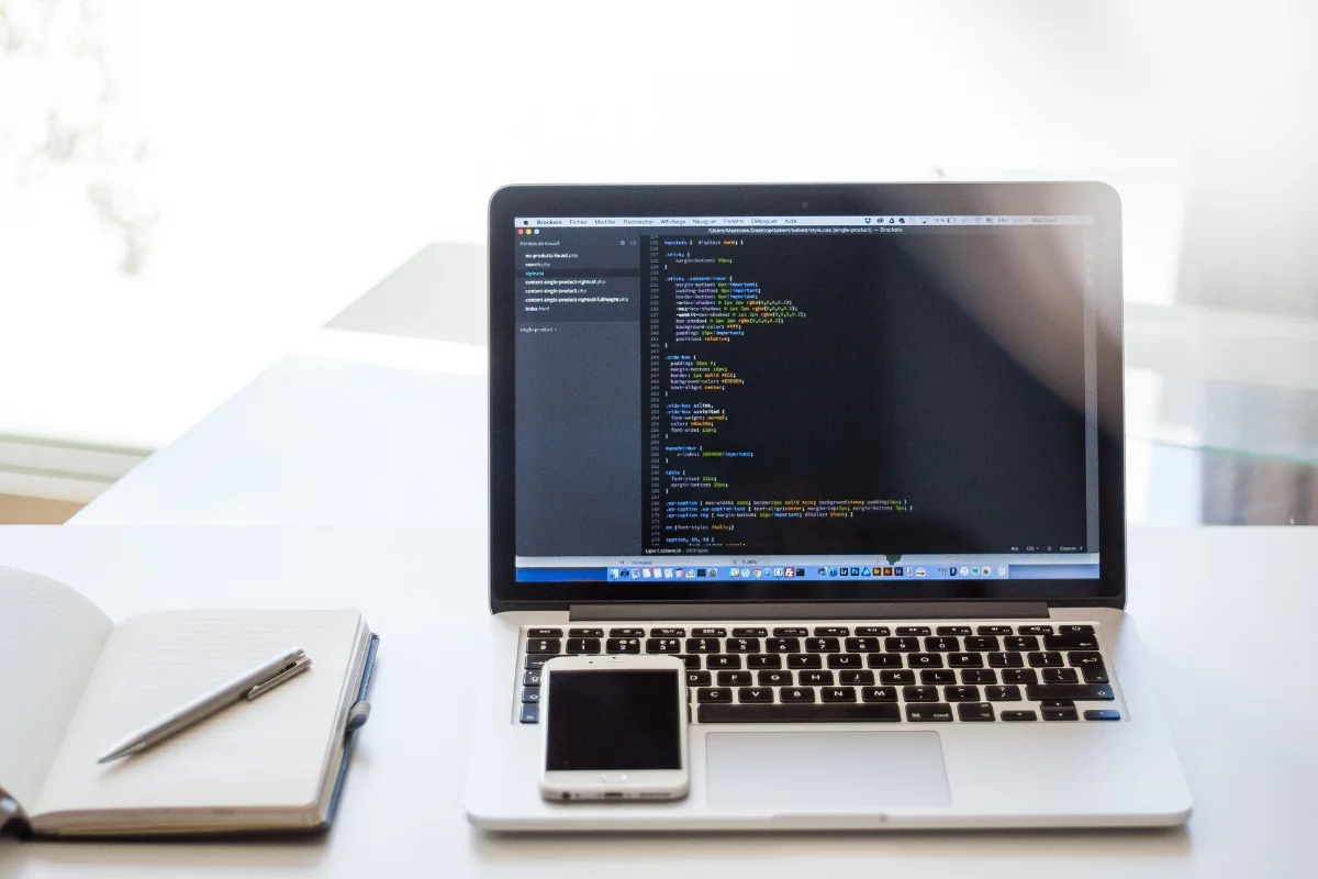 A laptop on a desk with a notebook and cell phone is common in many offices.
