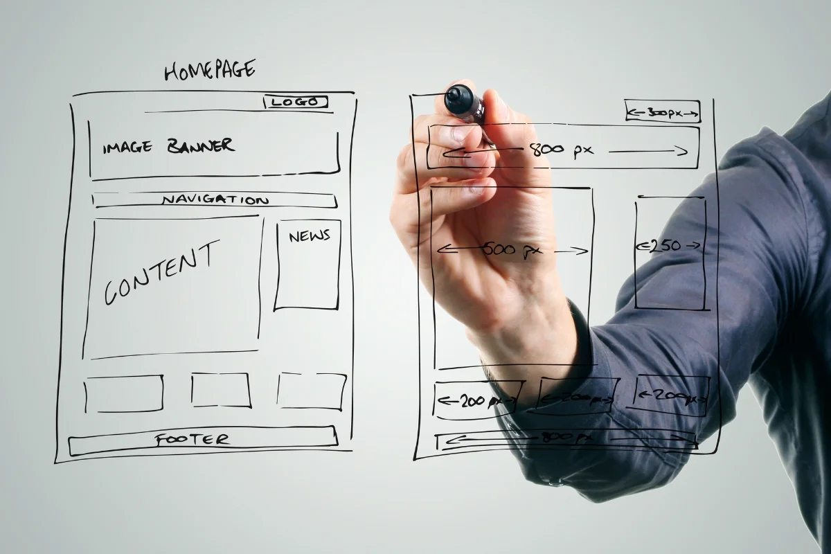 How to Create Wireframes: A Beginner's Guide for Stunning Designs 3 A person sketching how to create wireframes for a website layout on a transparent surface with markers.