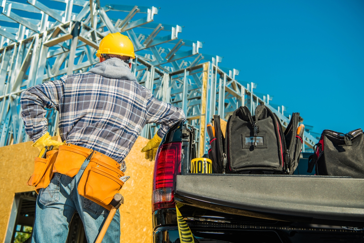 Construction worker with hard hat and tool belt next to a pickup truck at a construction site, embodying the efficiency marketed by construction companies.