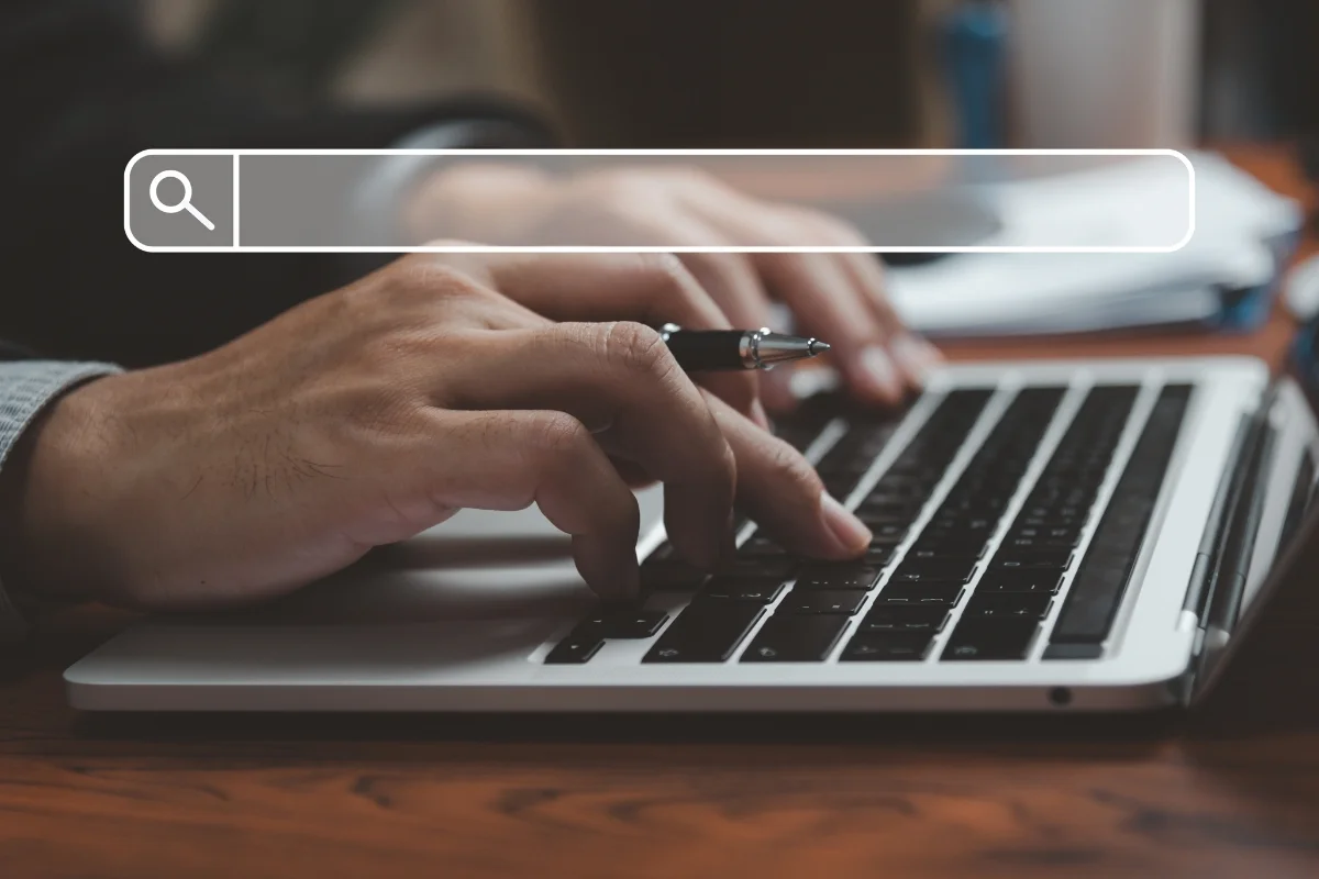 How to Search on a Website: Mastering the Art of Navigation 4 Close-up of a person's hands holding a pen and using a laptop with a "how to search on a website" graphic overlaying the image.