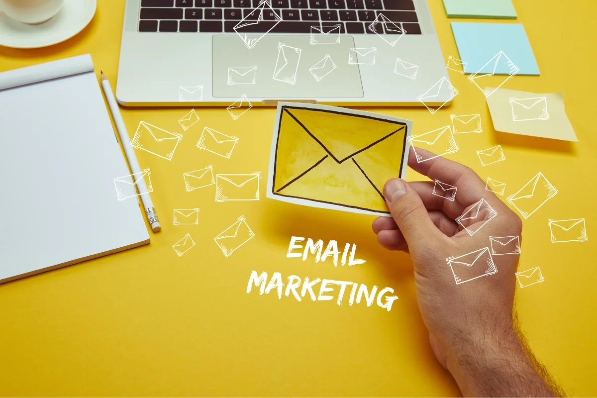 Email Marketing for Plumbers: Boost Your Plumbing Business Effectively 3 A hand holds an envelope icon in front of a laptop with floating email icons around, emphasizing the theme of email marketing for plumbers. A notebook, pencil, sticky notes, and a laptop are also visible.