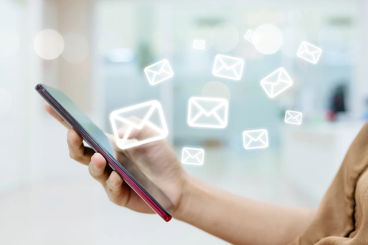 Email Marketing for Plumbers: Boost Your Plumbing Business Effectively 8 A person holds a smartphone with several envelope icons floating above, representing email messages being sent or received—showcasing the power of email marketing for plumbers.