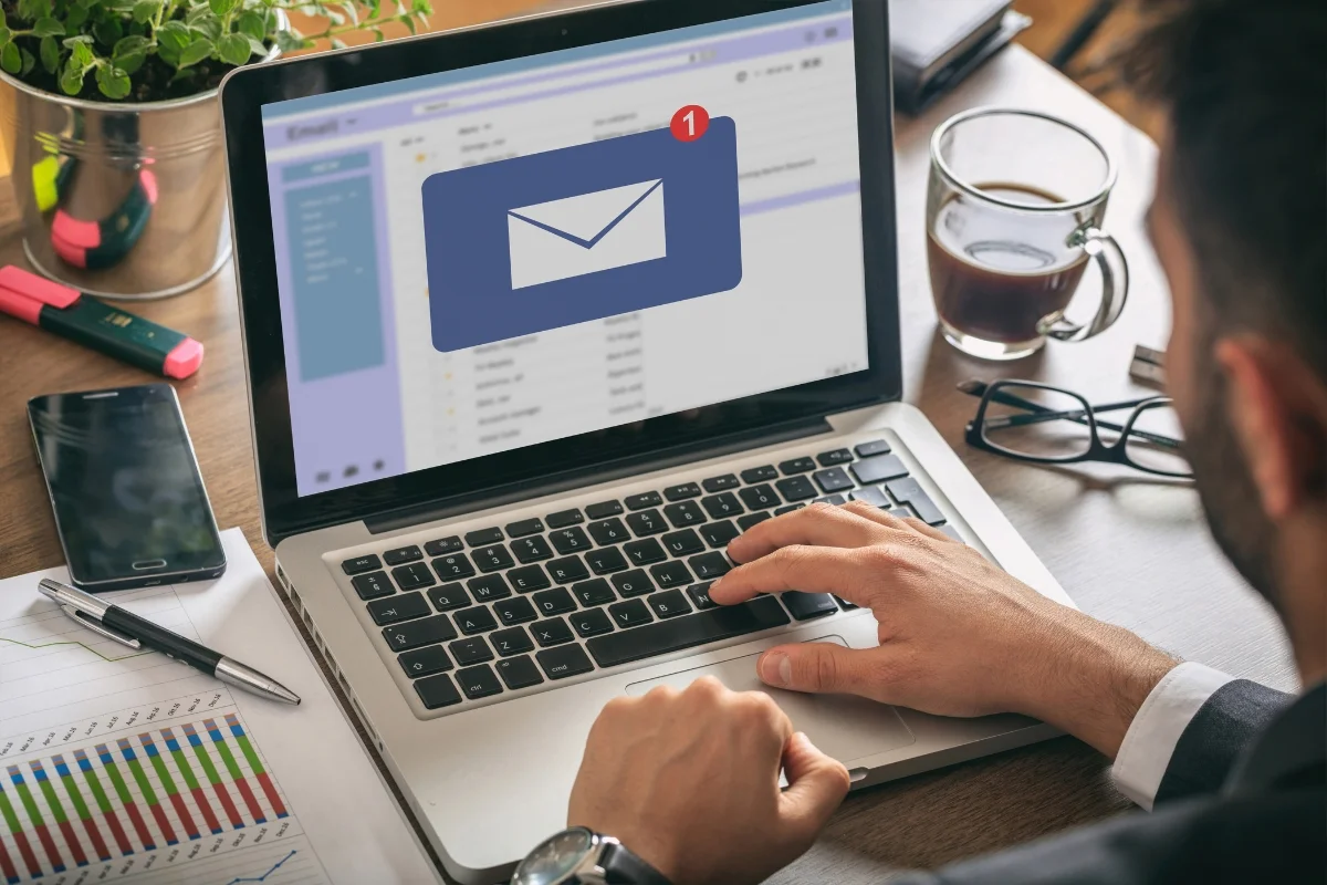 Email Marketing for Plumbers: Boost Your Plumbing Business Effectively 2 A person using a laptop with an email notification icon on the screen, indicating one new message. A coffee cup, charts on email marketing for plumbers, and office supplies are on the desk.