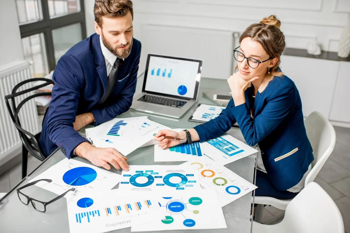 Plumbing Automation: Boost Customer Engagement Effortlessly 4 Two business professionals, specializing in plumbing automation, analyze charts and graphs at a desk with a laptop, wearing formal attire in a modern office setting.