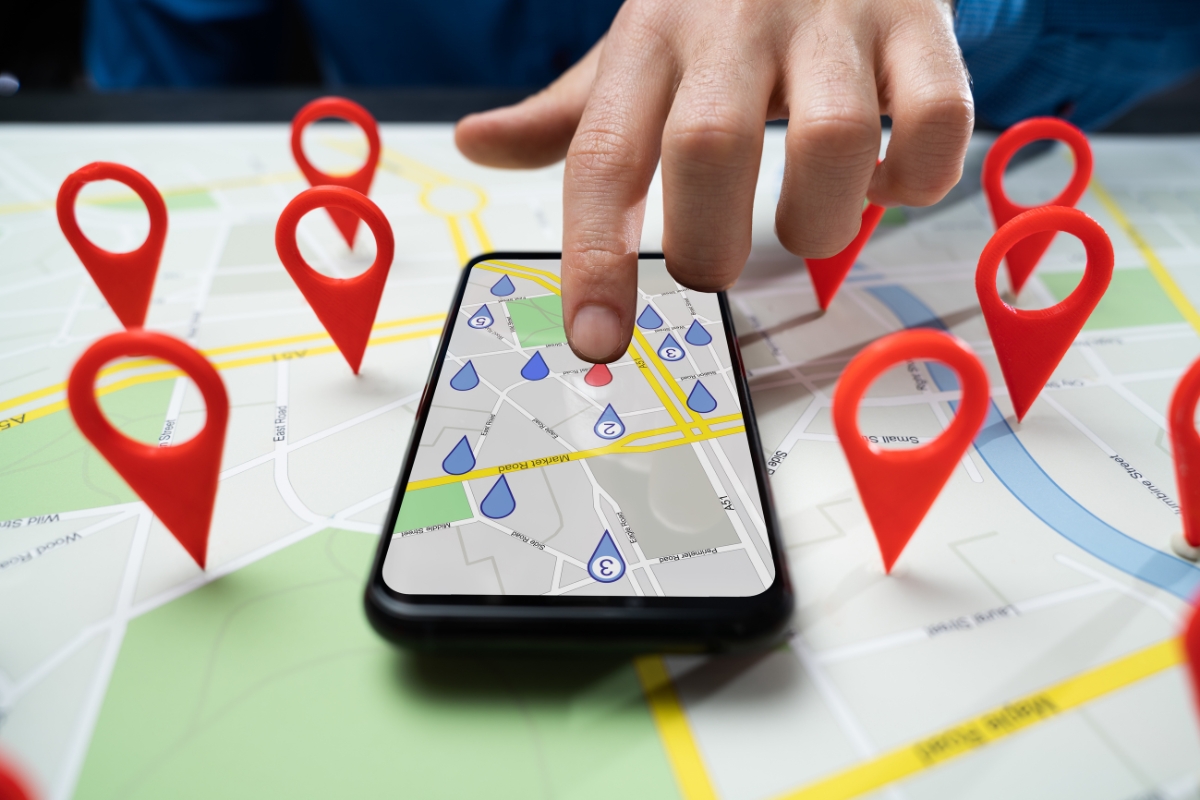 A hand points to a smartphone screen displaying a map with various pins, placed on a physical map also marked with red location pins, highlighting the service area pages.