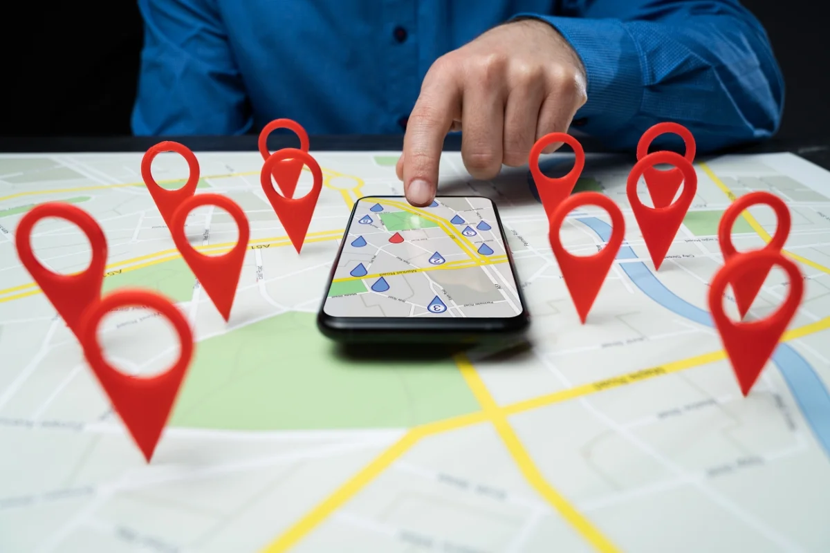 What Is Hyperlocal Marketing: Targeting for Local Business Growth 4 A person points at a map on a smartphone, surrounded by large red location markers on a physical map, illustrating the concept of What Is Hyperlocal Marketing.
