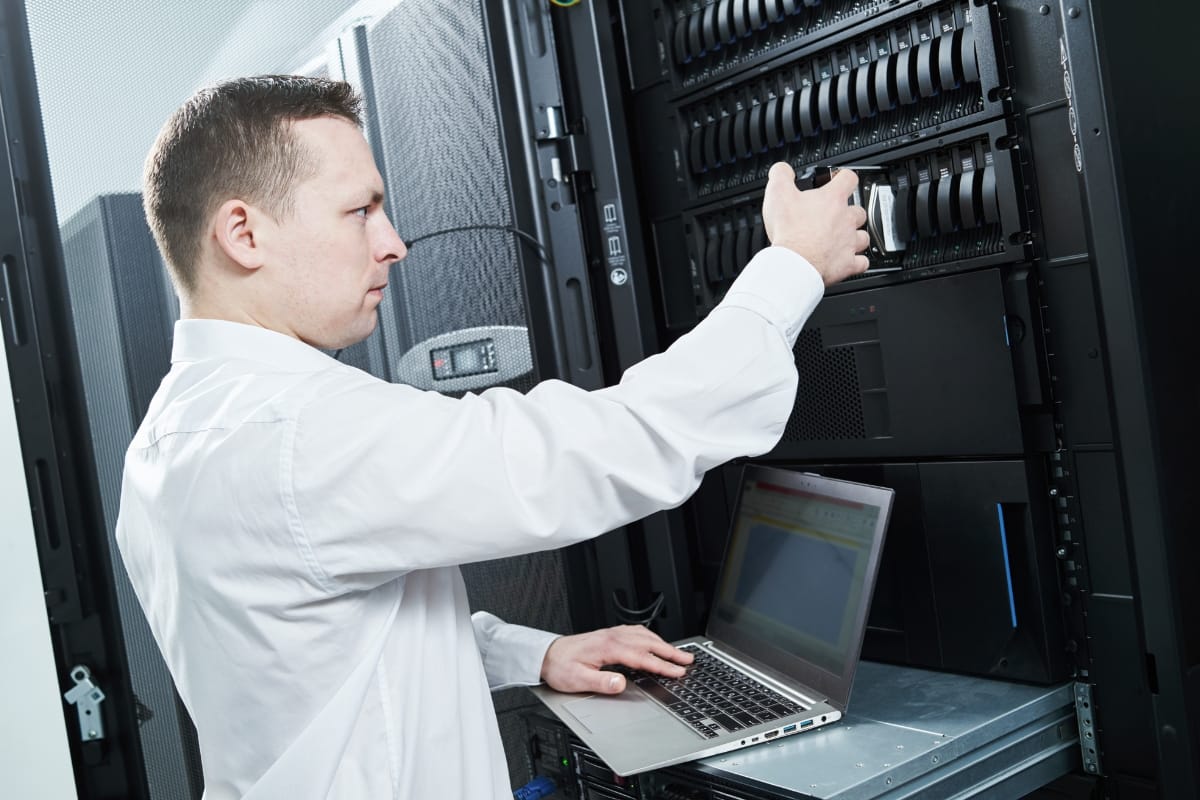 Must-Have Database Maintenance Plugins for WordPress 9 A person in a white shirt works on a laptop next to a server rack, skillfully adjusting equipment for database maintenance.