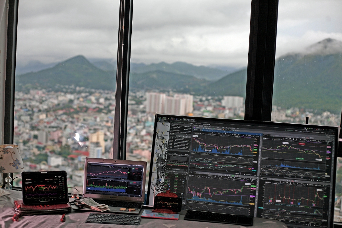 Blockchain in Digital Marketing: Potential Use Cases 3 Three monitors display stock charts and trading platforms on a desk by a large window, overlooking a cityscape with mountains in the background—highlighting how blockchain in digital marketing is transforming financial analysis and transparency.