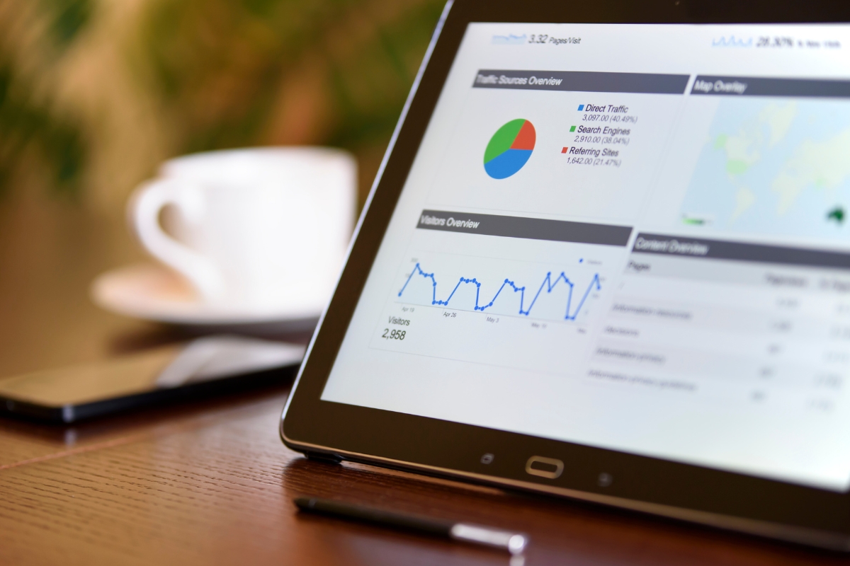 Understanding Google's Core Web Vitals and Its Impact on SEO 2 A tablet displaying core web vitals analytics charts and graphs sits on a wooden table next to a pen, a smartphone, and a blurred white coffee cup in the background.